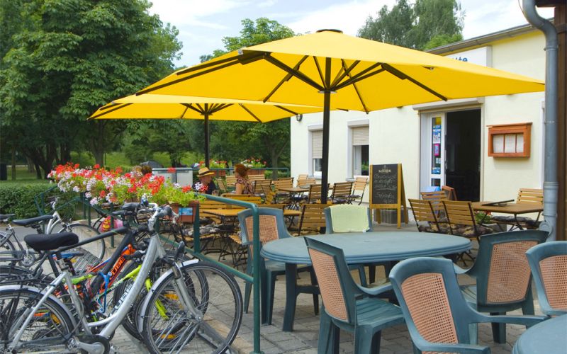 Kleiner Außenbereich der Gaststätte mit Tischen und Stühlen, zwei gelben Sonnenschirmen sowie einem Fahrradabstellplatz